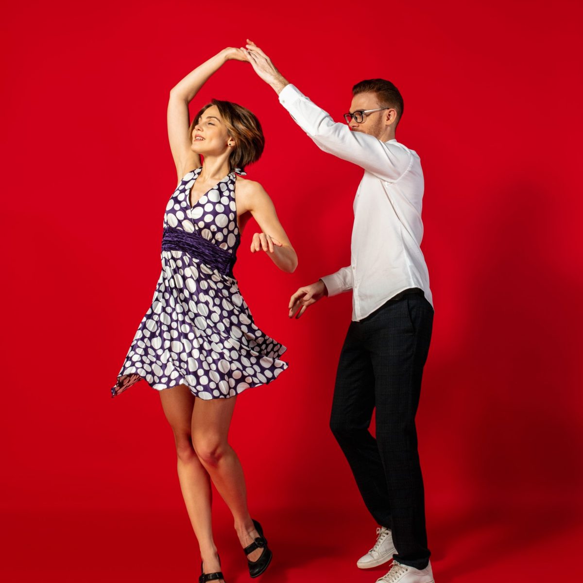 Rock n roll. Old-school fashioned young woman dancing isolated on red studio background. Artist fashion, motion and action concept, youth culture, fashion returning. Young stylish man and woman.